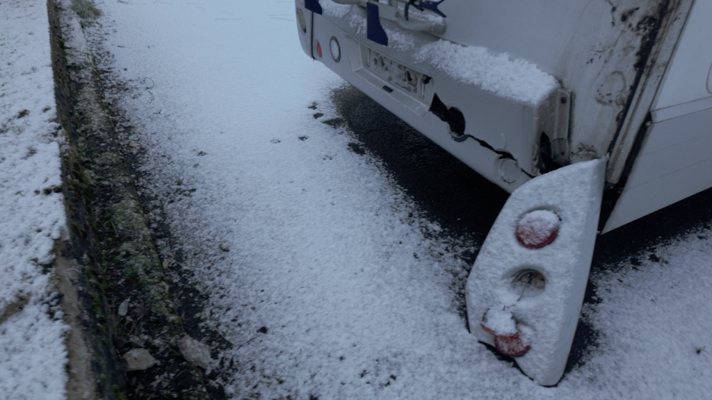 Rear bumper damage to a motorhome which hit a wall, viewed after a covering of snow.